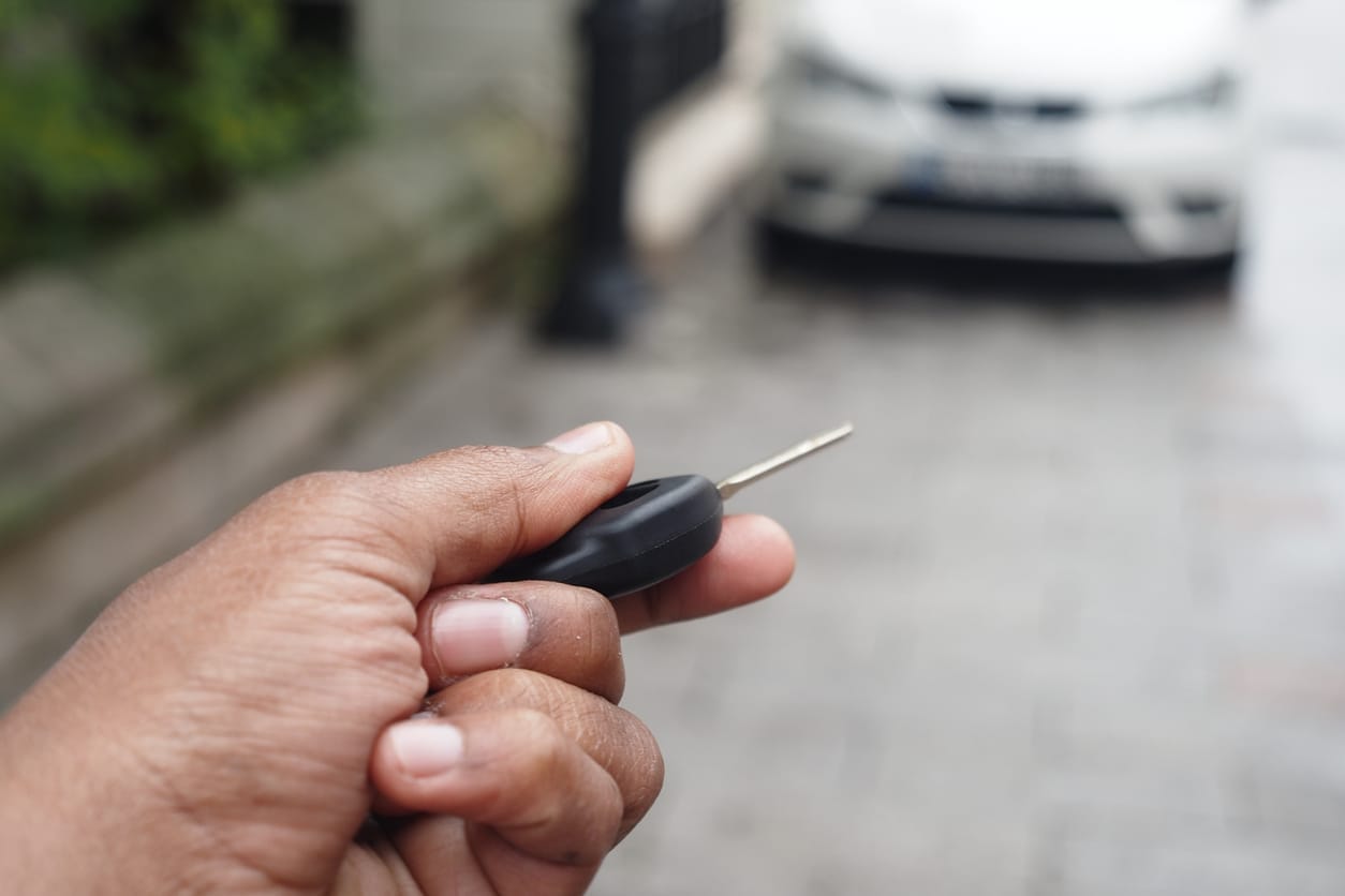 Hånd med bilnøkkel låser opp en hvit bil parkert i gaten